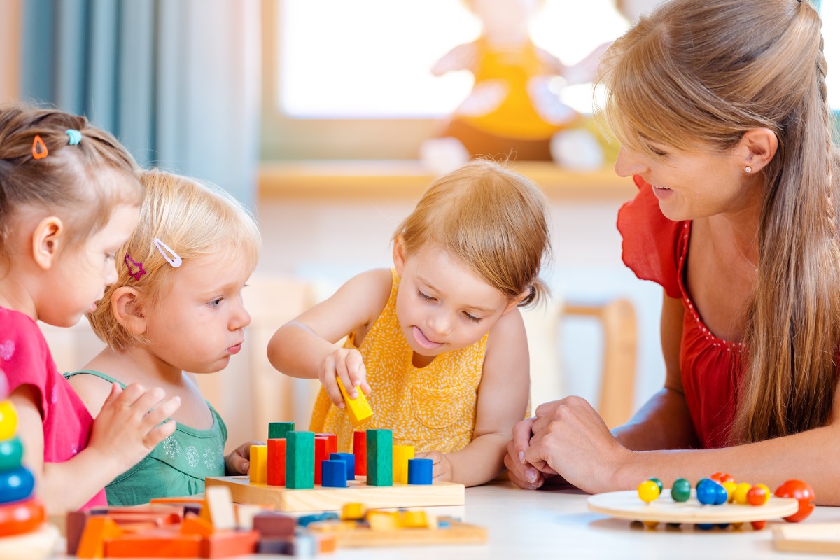 Kindergartenpädagogin spielt mit Kindern die Bausteine stapeln